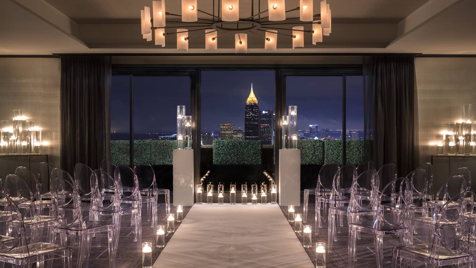 Translucent chairs are arranged in rows and candles line a pathway to the front of the ballroom
