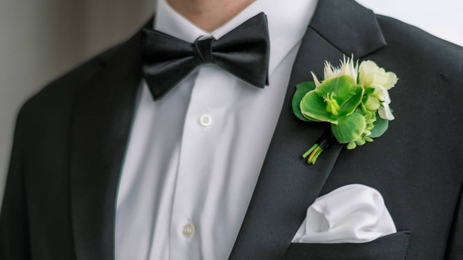 Close up of a groom's tuxedo, with white silk pocket square and green and white boutonni�re