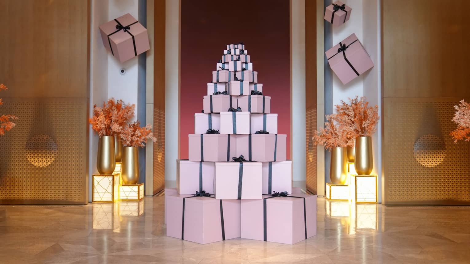 Pink present boxes with black ribbon are stacked in the shape of a tree in a hotel lobby