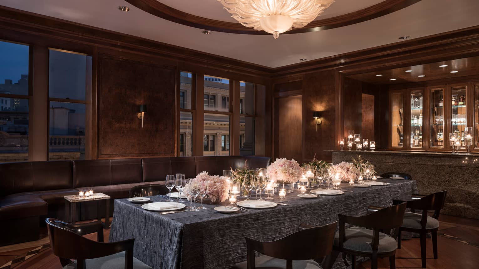 Elegant, candle-lit dining table in private den with grey tablecloth, pink flower arrangements, wine glasses