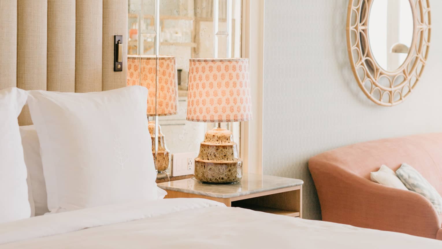 Elegant hotel room with a plush white bed, mirrored headboard, stylish lamps on nightstands, and a round decorative mirror on the wall. 