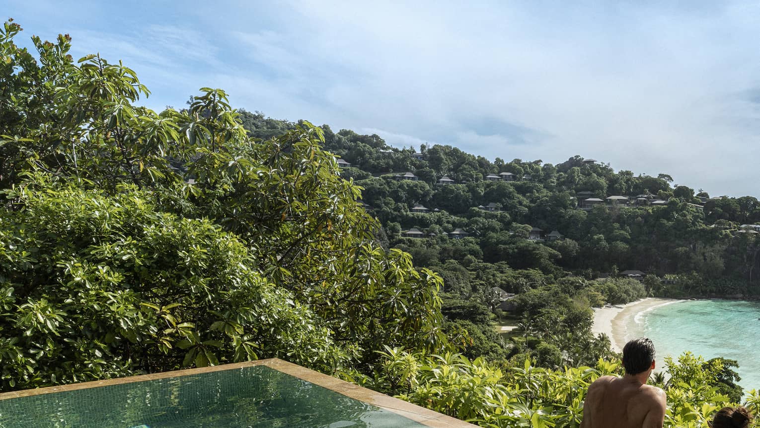 A couple looks out at a view of crystal blue waters and cliffs from an infinity pool