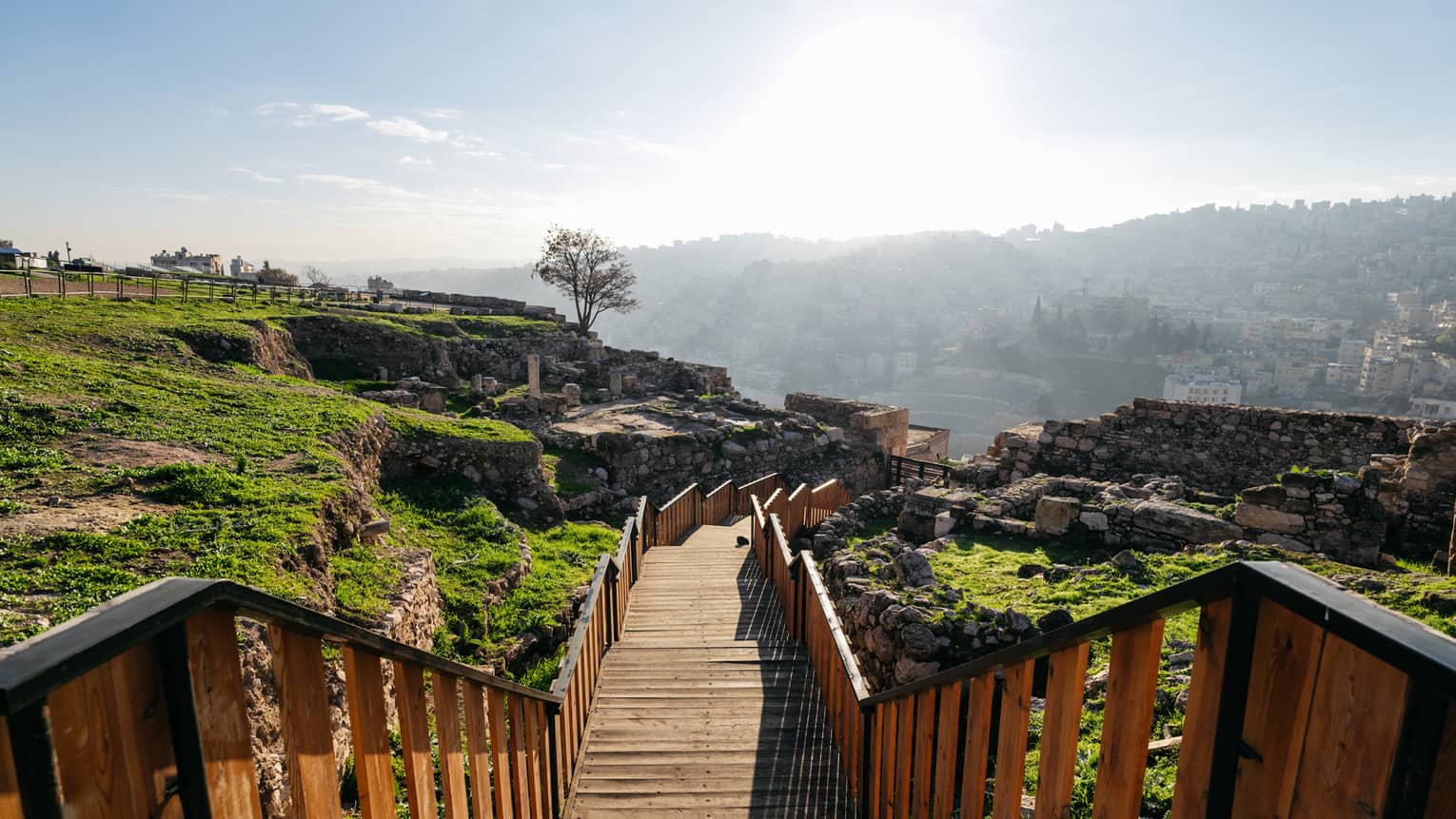Long wooden walkway leads from a rocky hilltop down to a city below