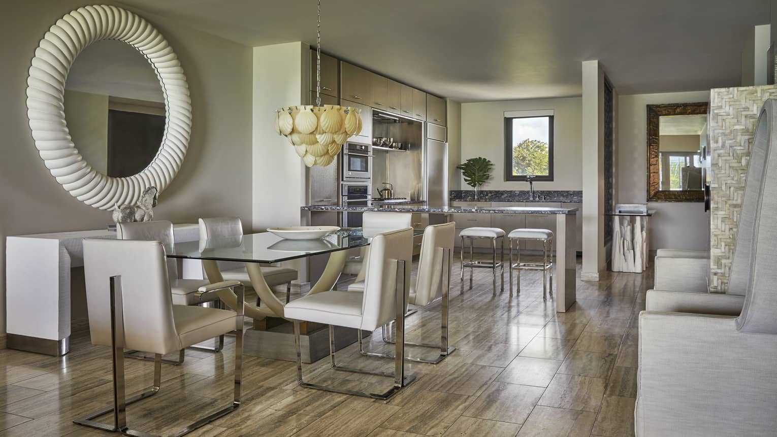 Three-bedroom penthouse dining room with glass table, white chairs, round white mirror, shell chandelier 