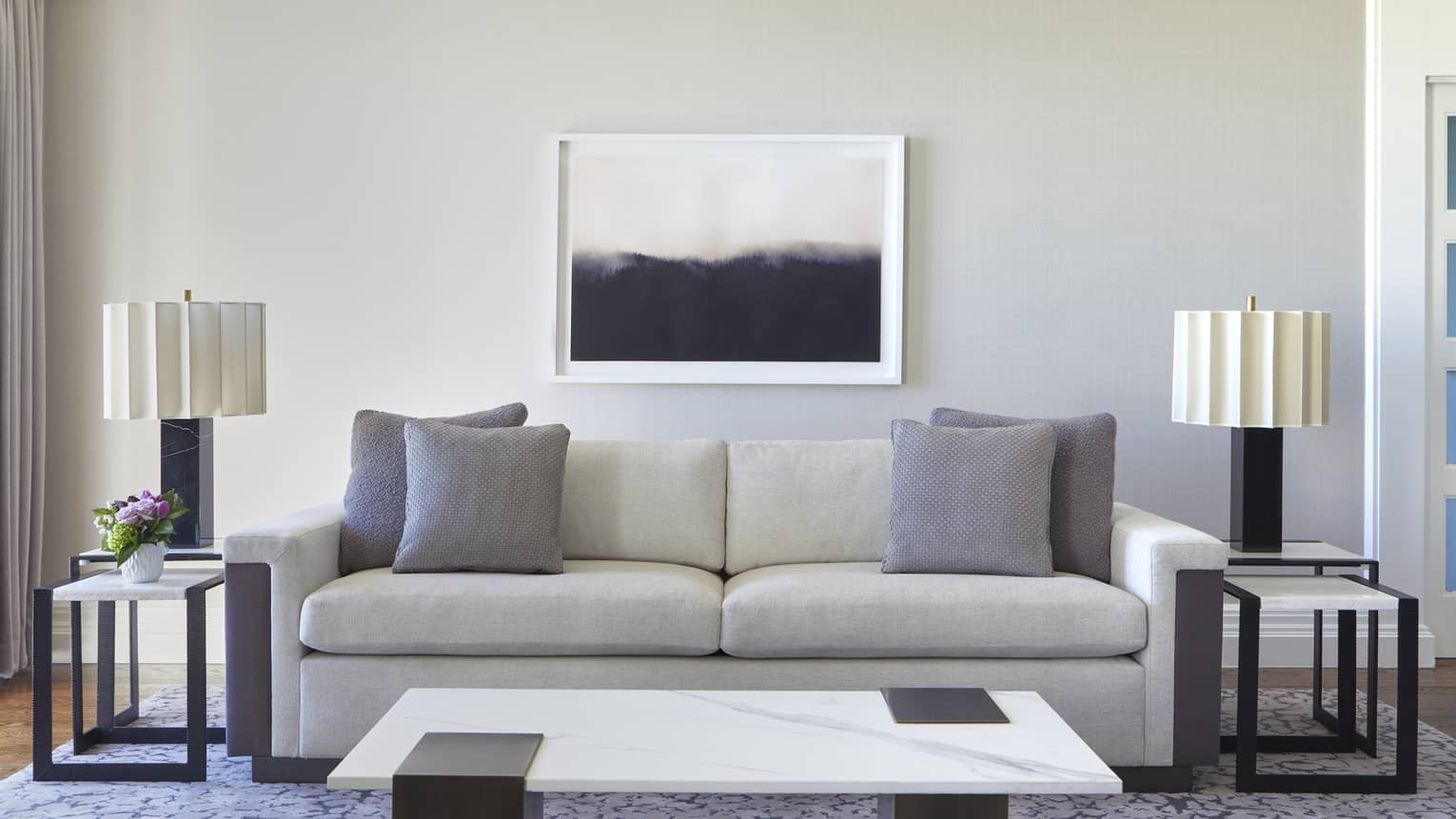 Living room with white sofa, grey pillows and rug, marble coffee table, and artwork hanging on the light grey wall