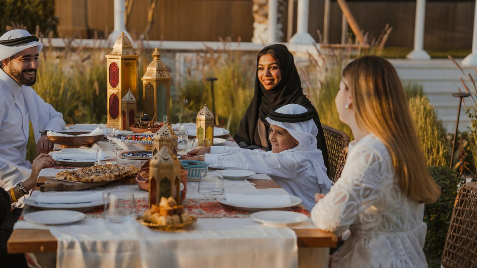A family of five sits at an outdoor table set for a Ramadan meal at sundown