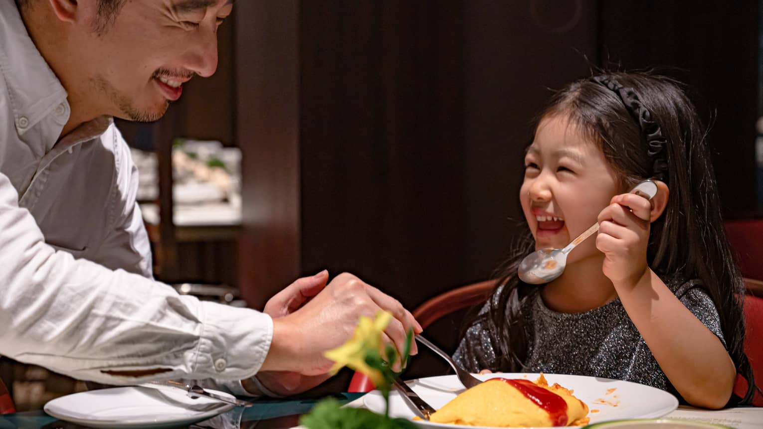 Smiling young girl and her dad dig into omurice topped with ketchup