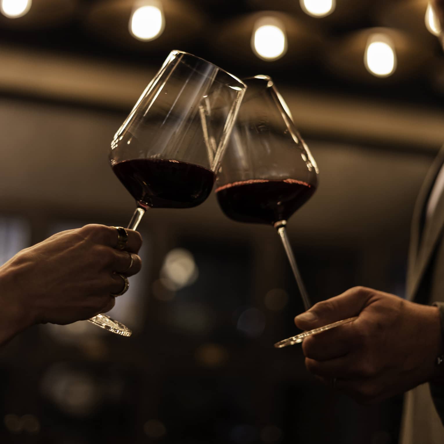 Two guests holding wine glasses with lights in the background.