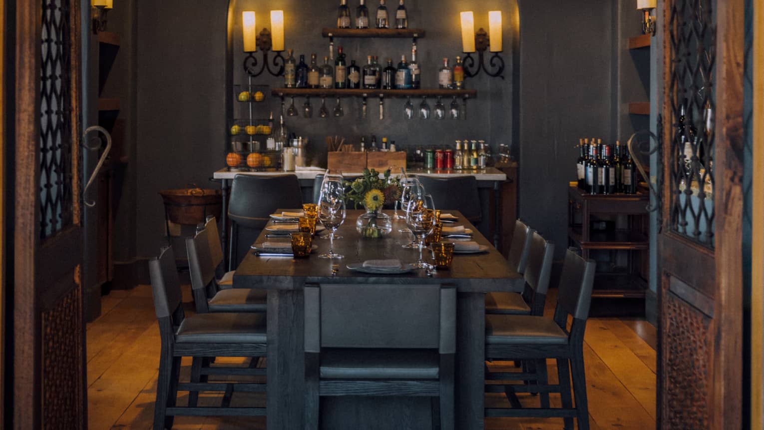 Entrance to a dining room with wooden doors and floors, and candle light chandeliers.