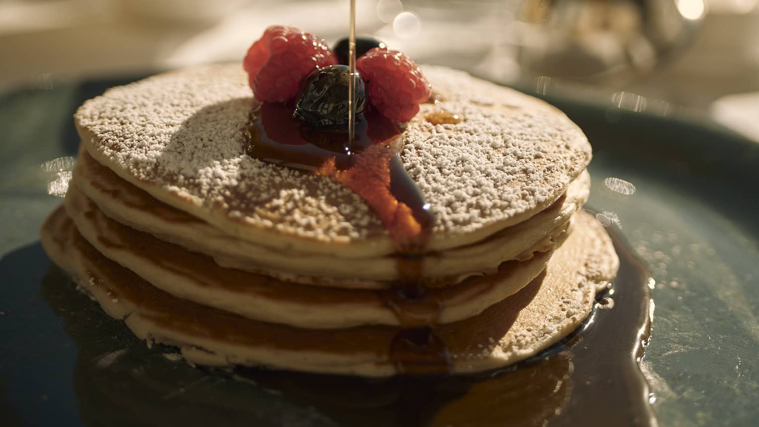 A stack of pancakes with berries and maple syrup