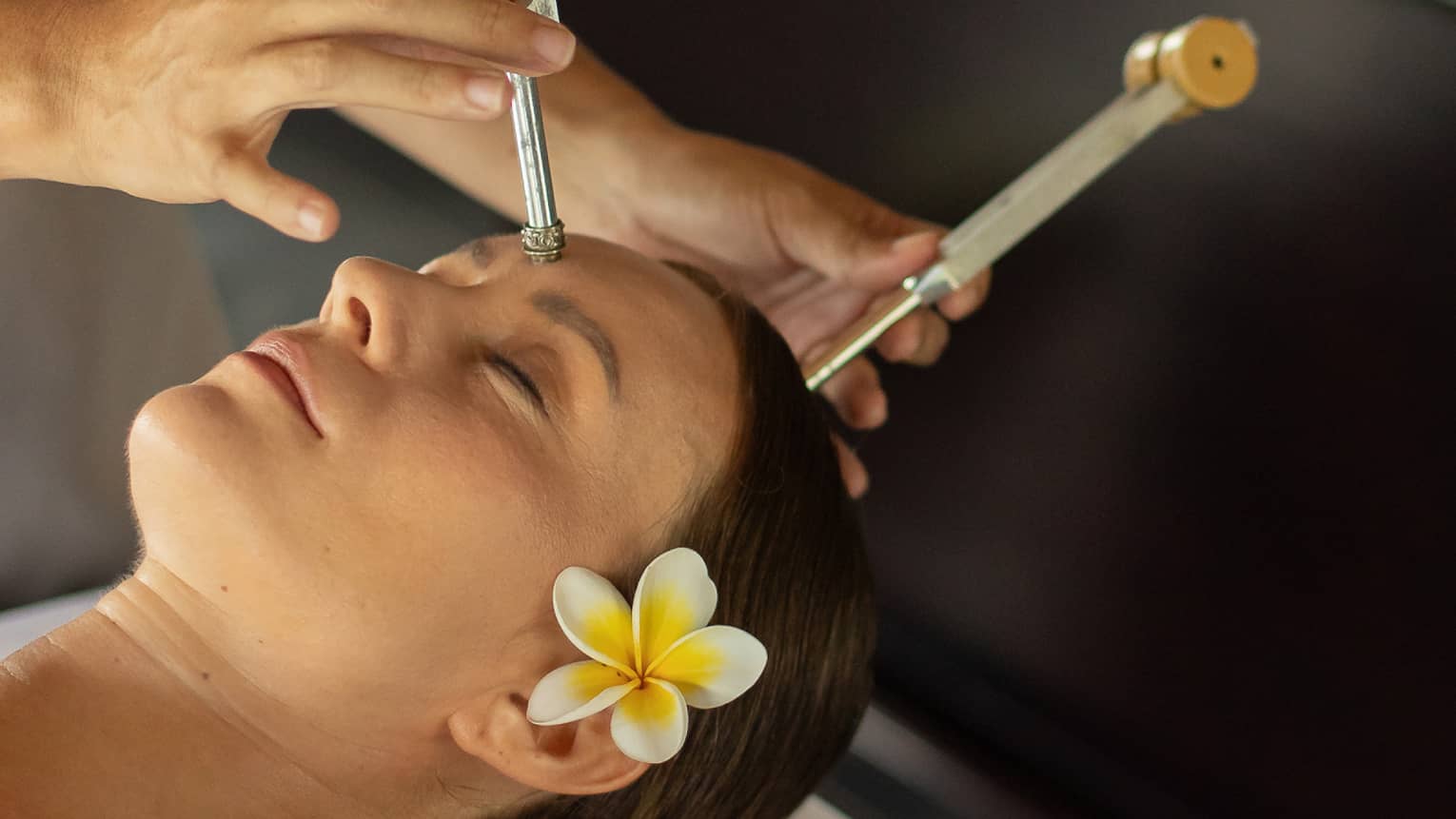 A practitioner delicately applies ohm tuning forks to the forehead and crown of a guest resting peacefully on a massage bed.