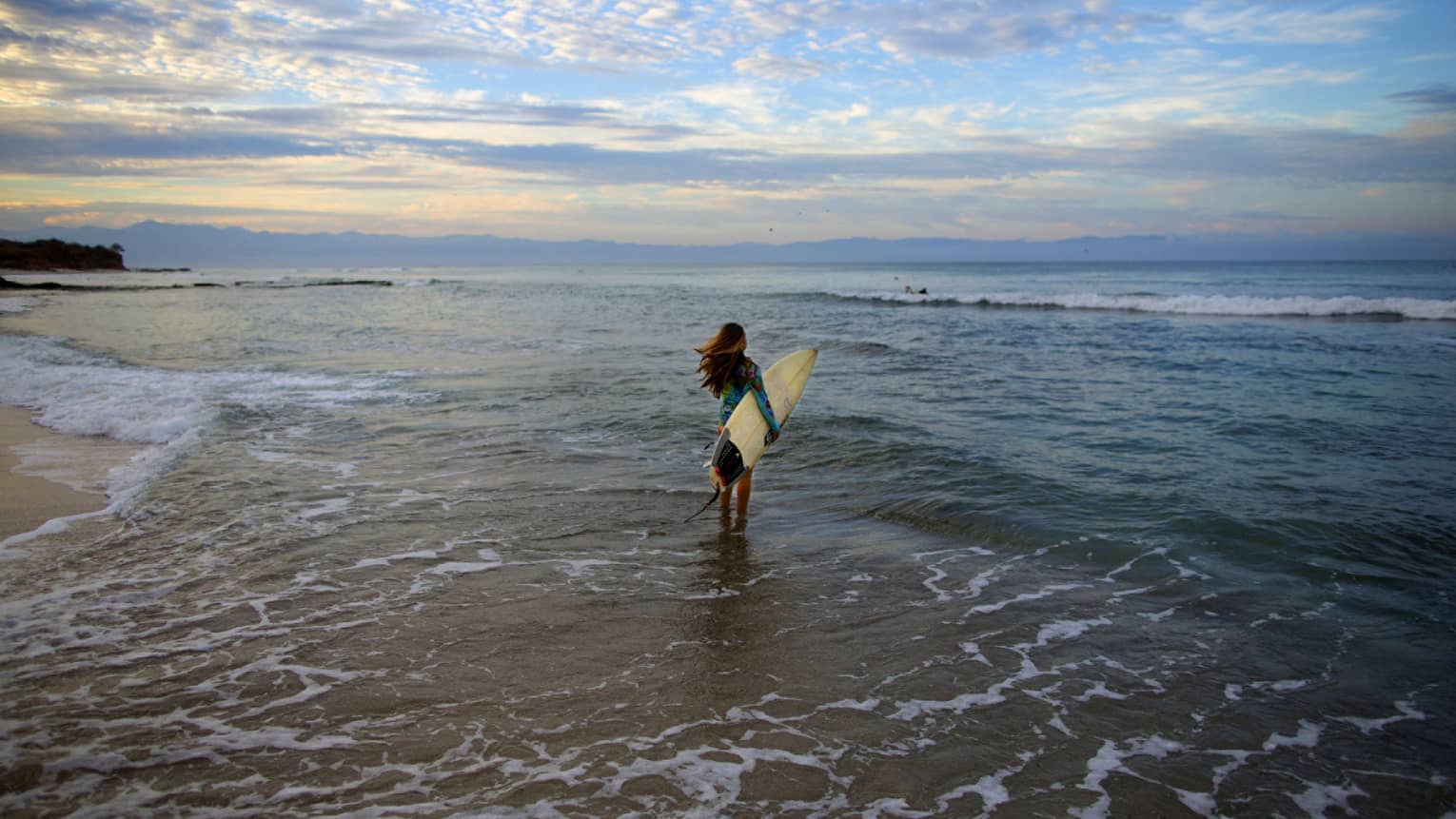 A woman holding a surfboard while walking towards ocean waves.
