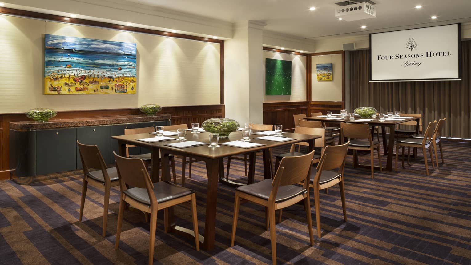 Gallery meeting room with small square tables with retro-style chairs, colourful paintings on walls