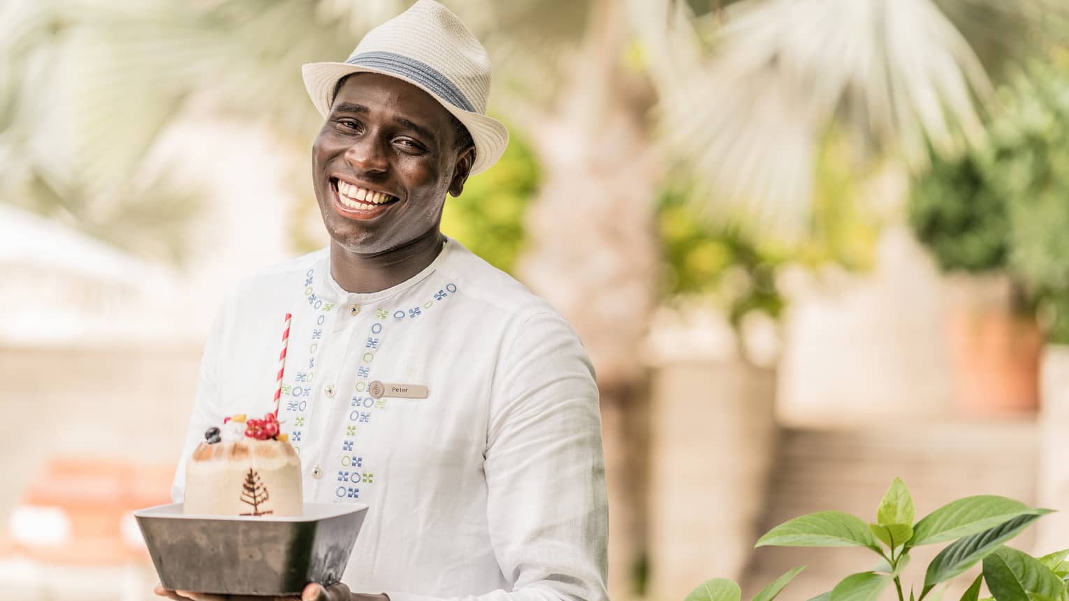Pool staff member in white tunic and fedora holding ice cream dessert with striped straw