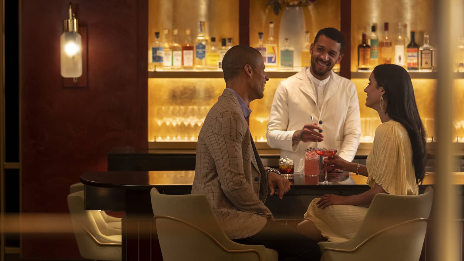 A couple enjoys cocktails at a bar served by a smiling bartender