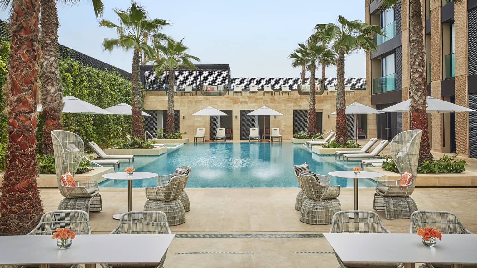 Courtyard pool flanked by tables and chairs with umbrellas, palm trees