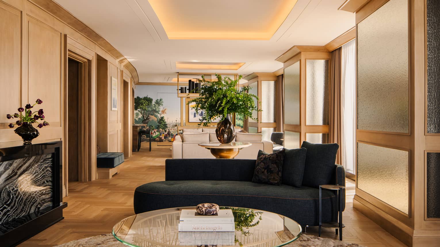 Contemporary luxury hotel suite living room, featuring a black sofa, glass coffee table and illuminated ceiling