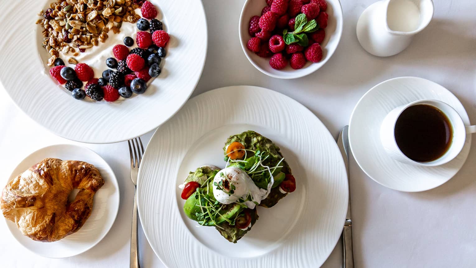 An assortment of food including avocado toast, yogurt, berries, and bread.