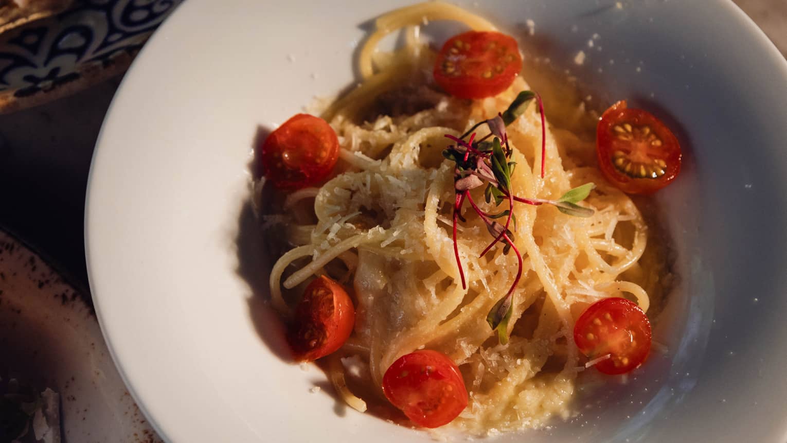 A round white shallow bowl containing a pasta dish with cherry tomatoes and other garnishes