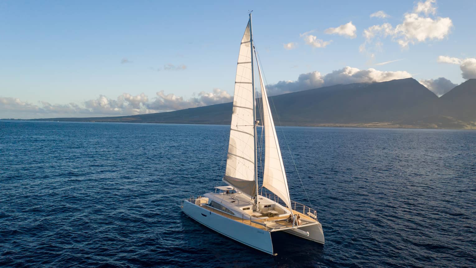 Catamaran sailing on the open water against a mountain backdrop