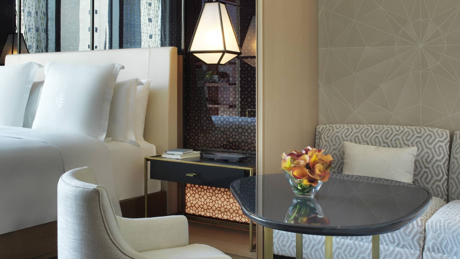 Close-up of modern plush white dining chair in front of bed with white linens 