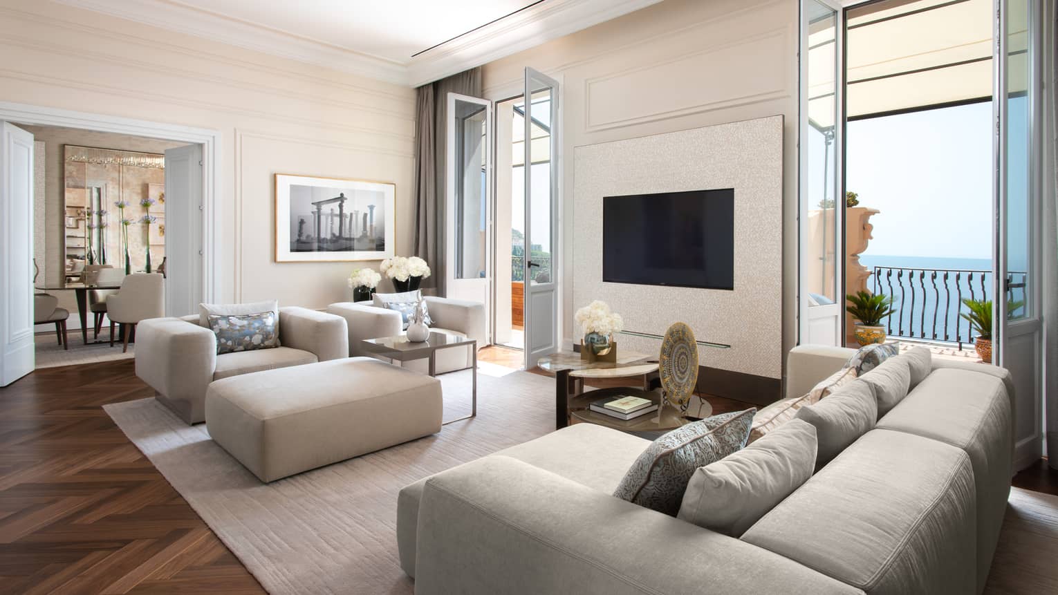 Living room with grey sofa, arm chair and ottoman, two doors opening to sea-view terrace