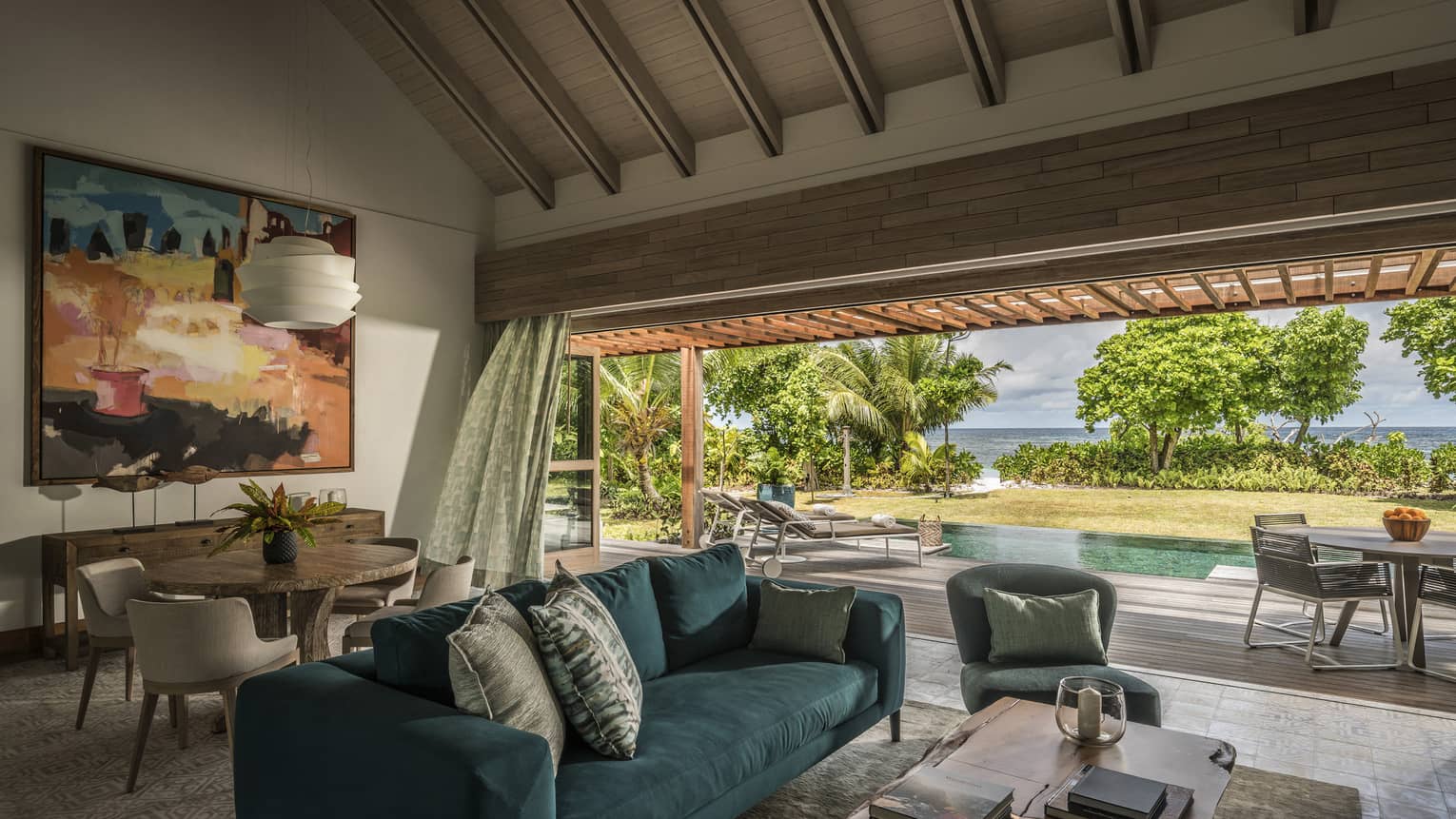 A blue couch sits in the middle of a sitting room overlooking a pool, with the ocean in the distance