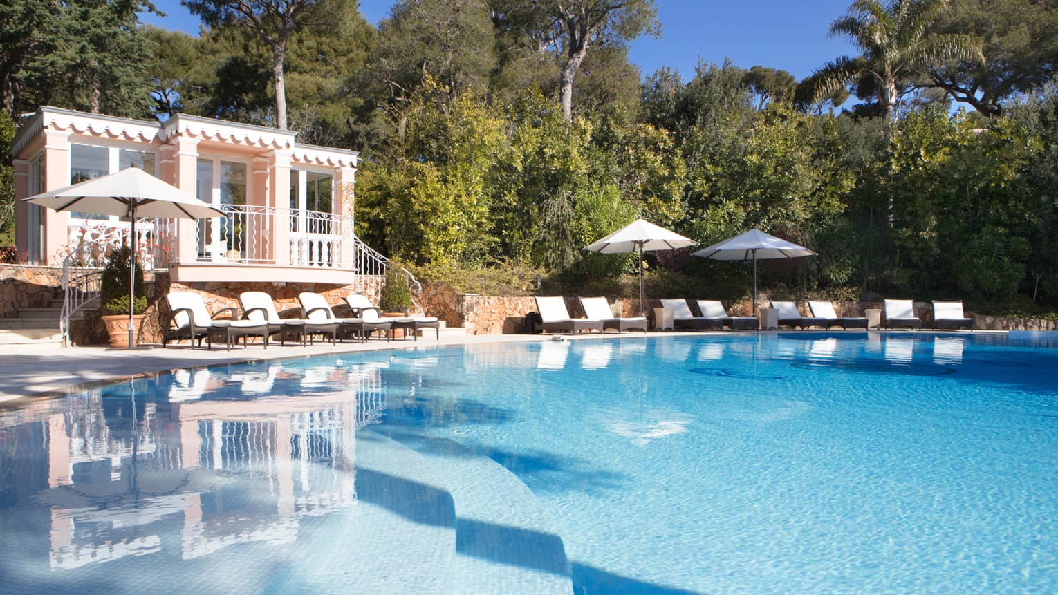 View over blue outdoor swimming pool to deck chairs, villa