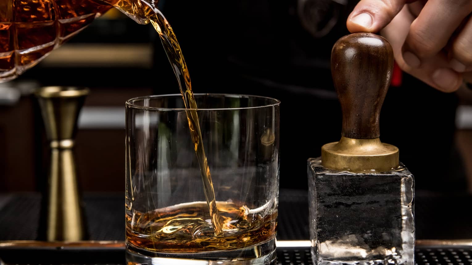 A bartender pouring whiskey into a glass.