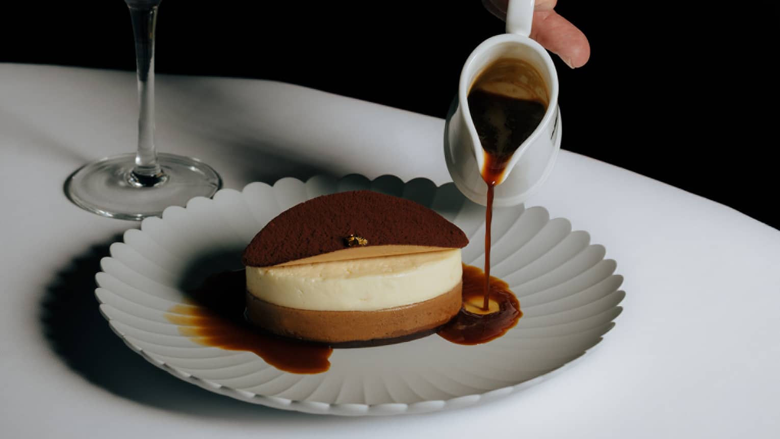 Tiramisu served on a white plate as a server pours syrup on the plate and an espresso martini sits nearby