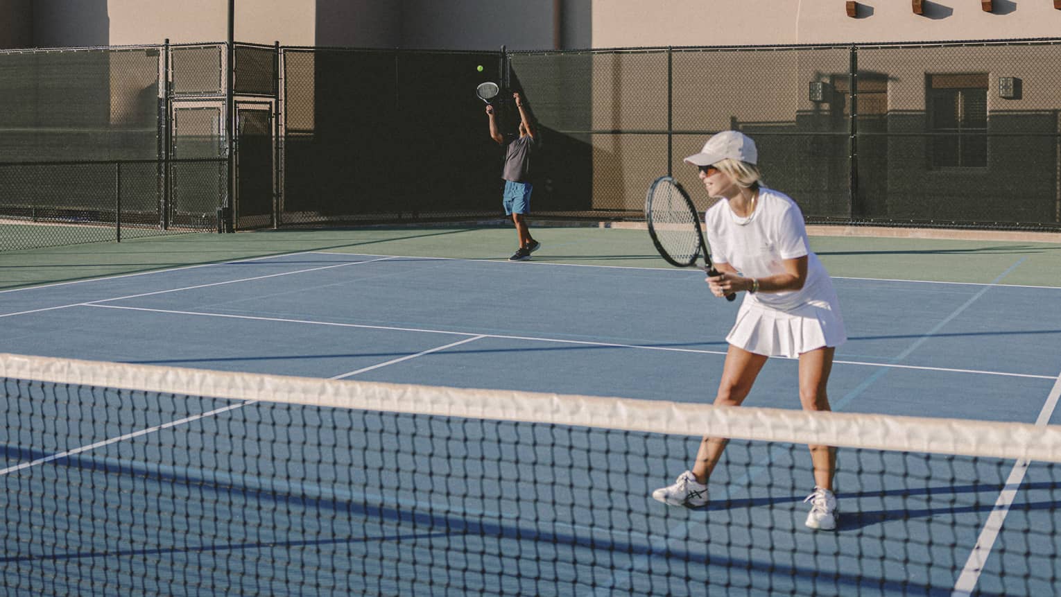 Two guests playing tennis on an outdoor tennis court.