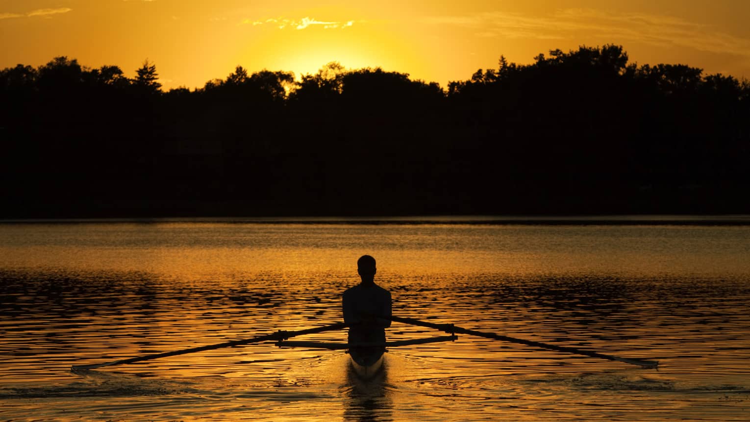 Silhouette of person on water in kayak at sunset
