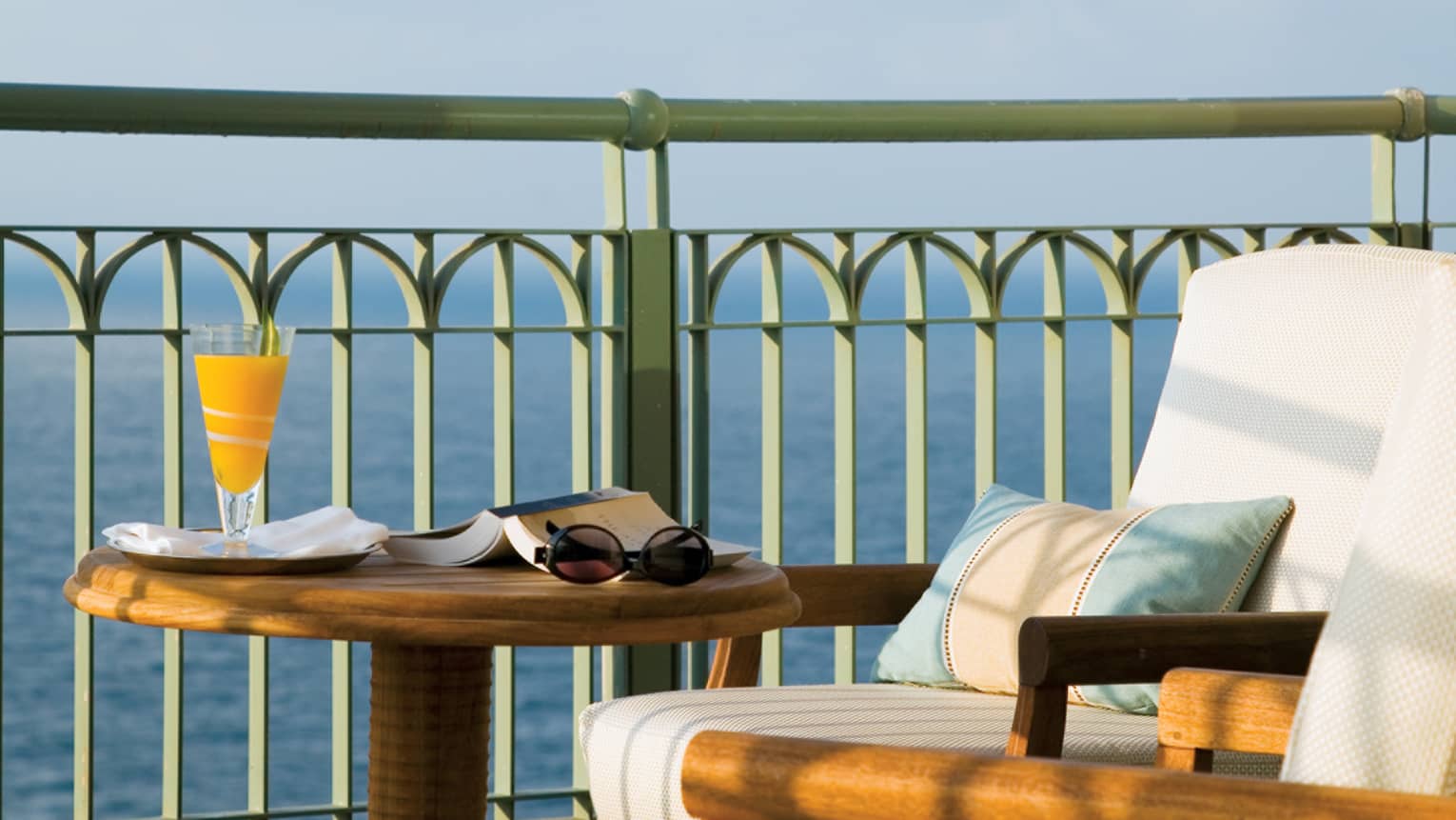Close-up of Presidential Suite patio round wood table with open book and orange juice, chair cushion, ocean view