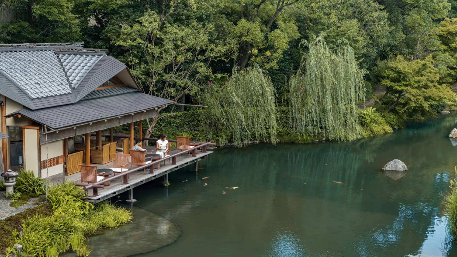 Two guests sit on the outdoor terrace of a pagoda overlooking the koi pond