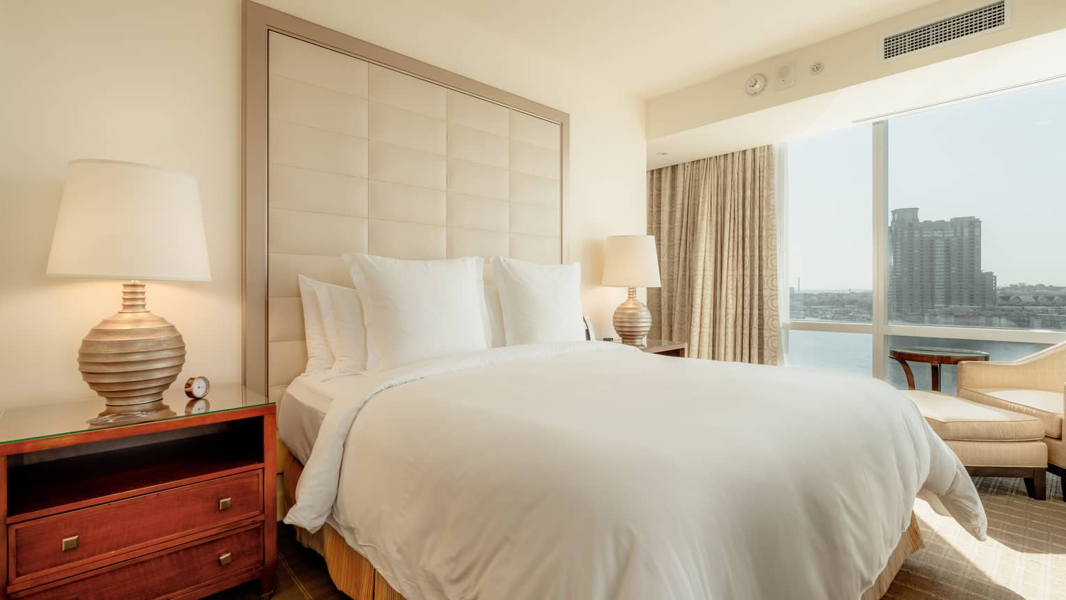 A guest room with floor-to-ceiling windows, two side tables with lamps and a view of the city