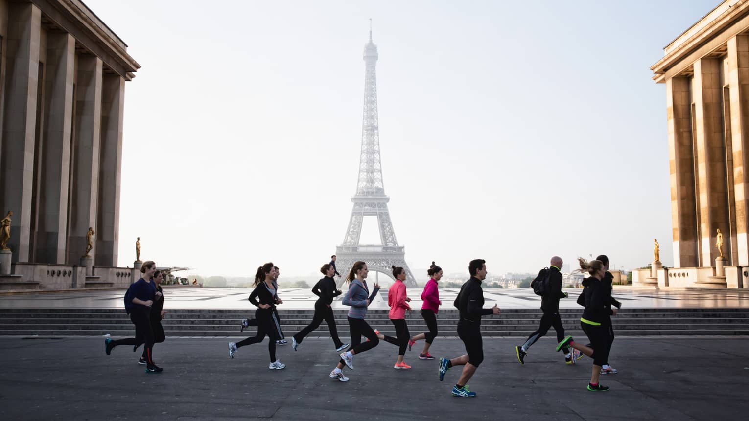 Group of runners jogs past Eiffel Tower on brick path