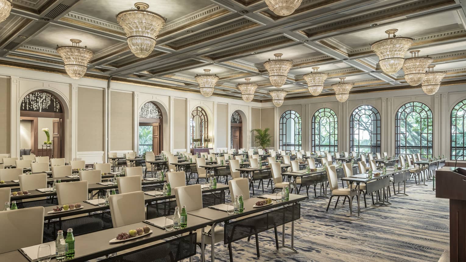 Bright, open ballroom with chandeliers and seats arranged facing forward, drinks and fruit on table