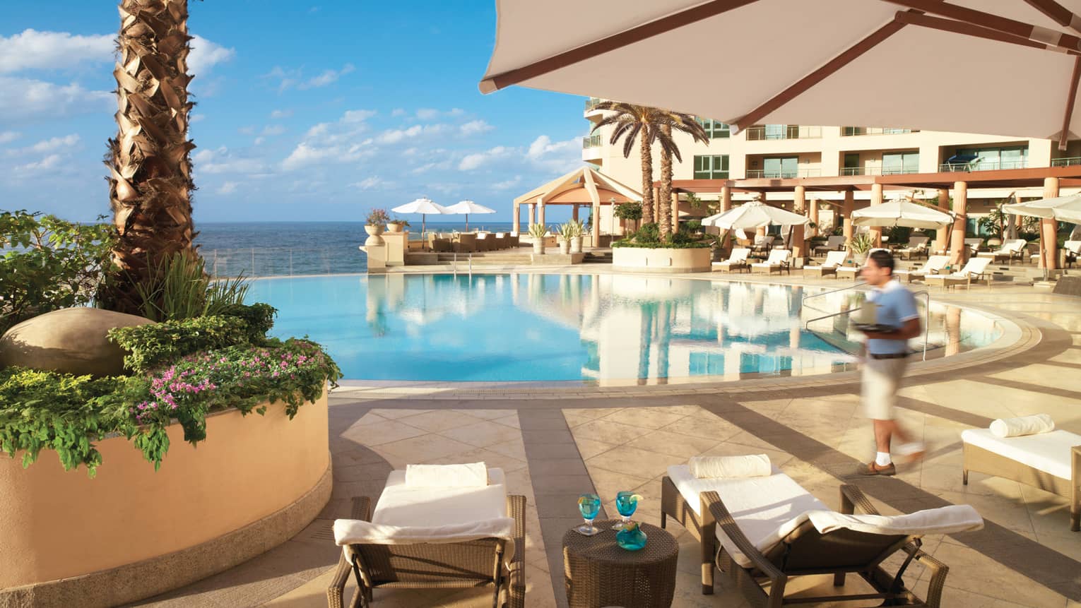 Two brown wicker deck chairs with white towels, blue drinks by hotel swimming pool, ocean view 