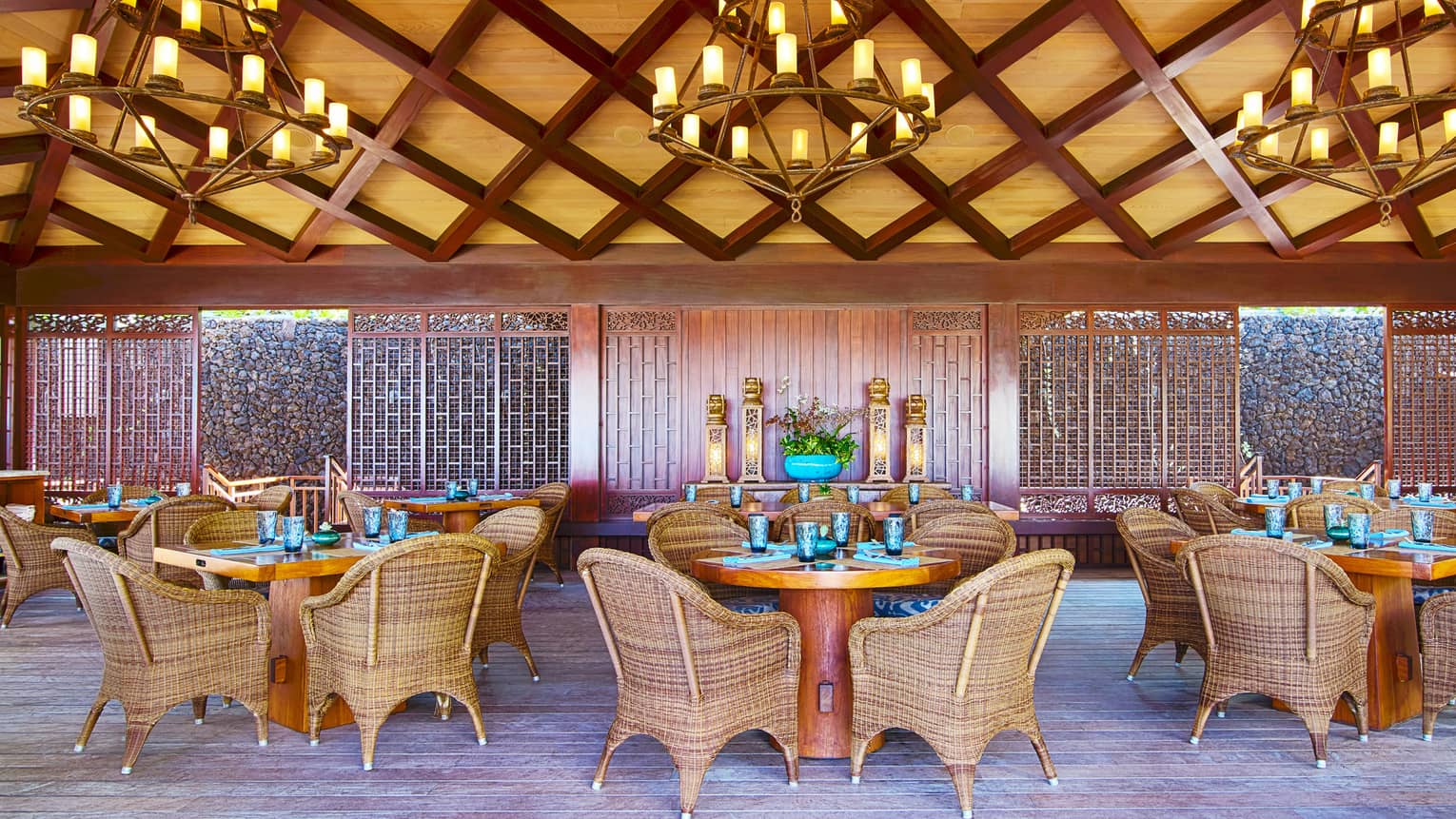 Dining area under bamboo and lattice ceiling with three chandeliers, round dining tables and wicker chairs