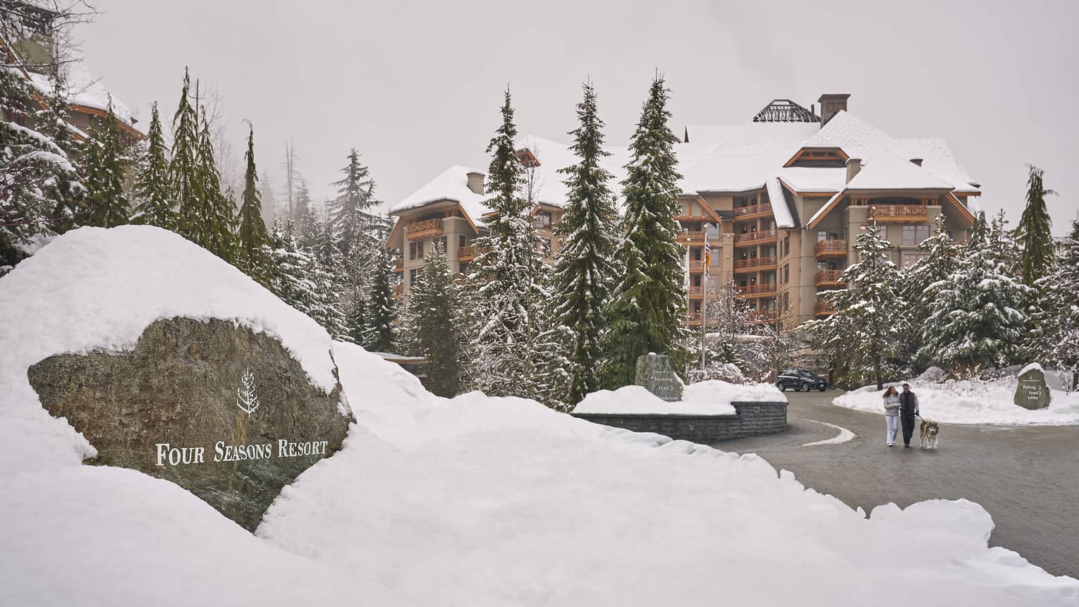 The entrance to Four Seasons Whistler covered in snow, and surrounded by tall pine trees.