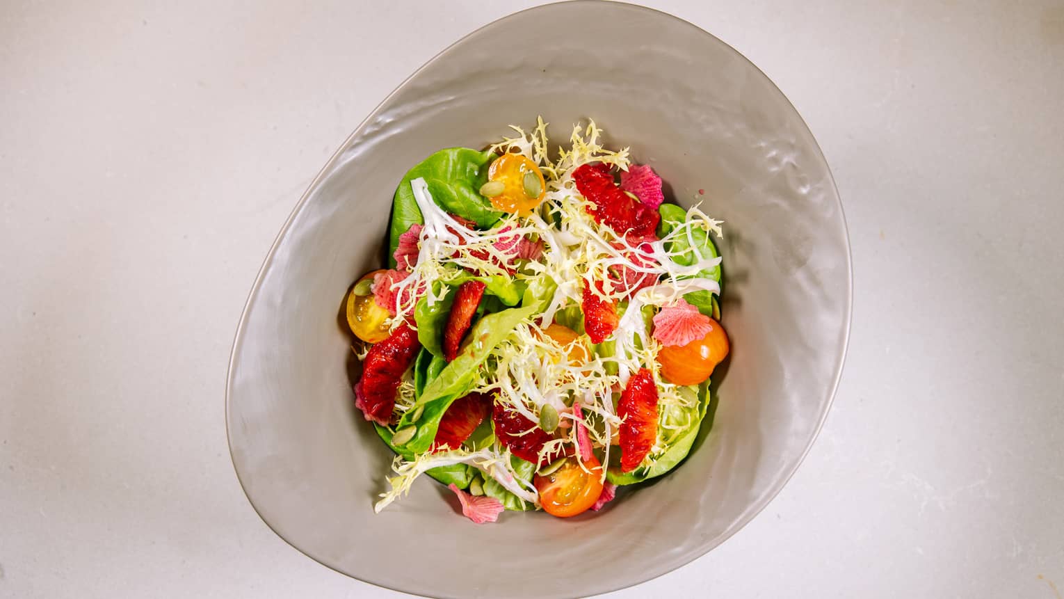 A garden salad with tomatoes in a grey bowl.