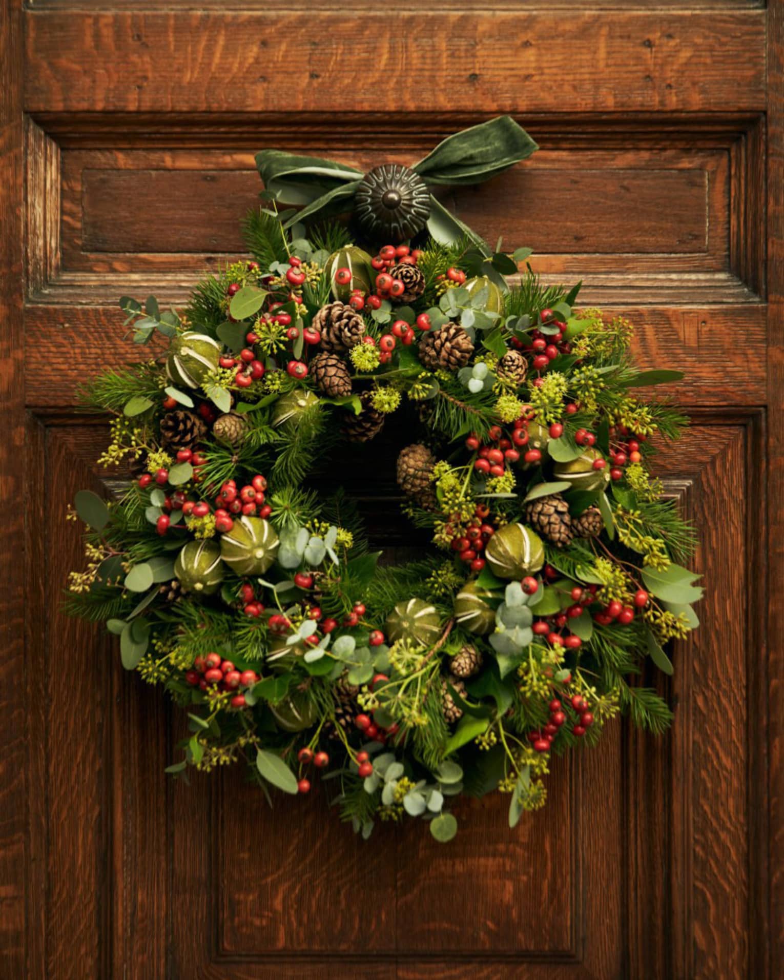 A wreath with red berries hanging on a wood door.