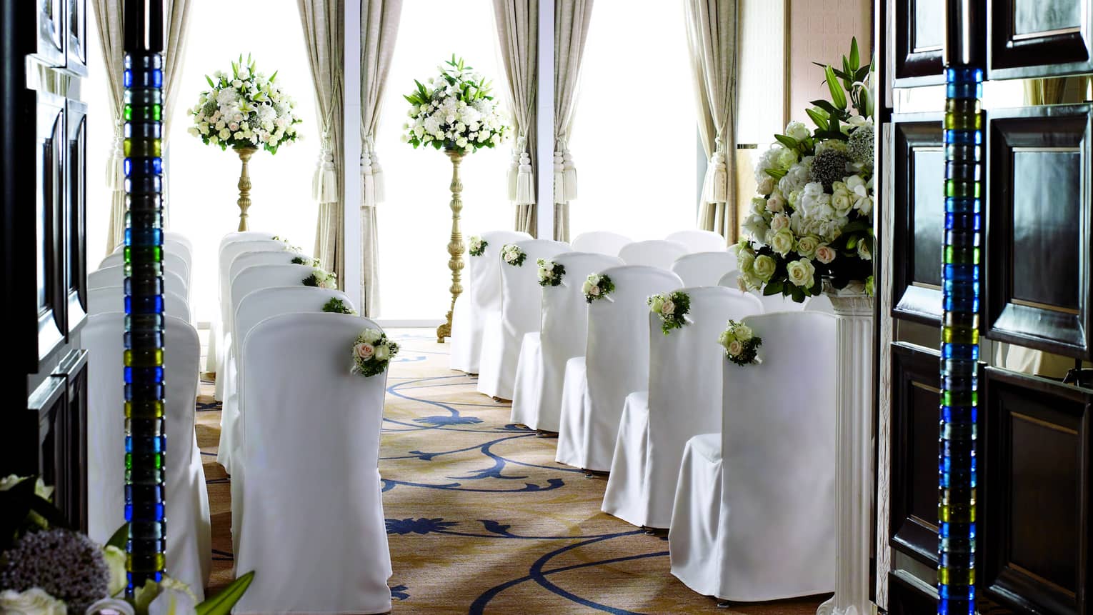 Ballroom wedding ceremony, rows of chairs with white linens face sunny window