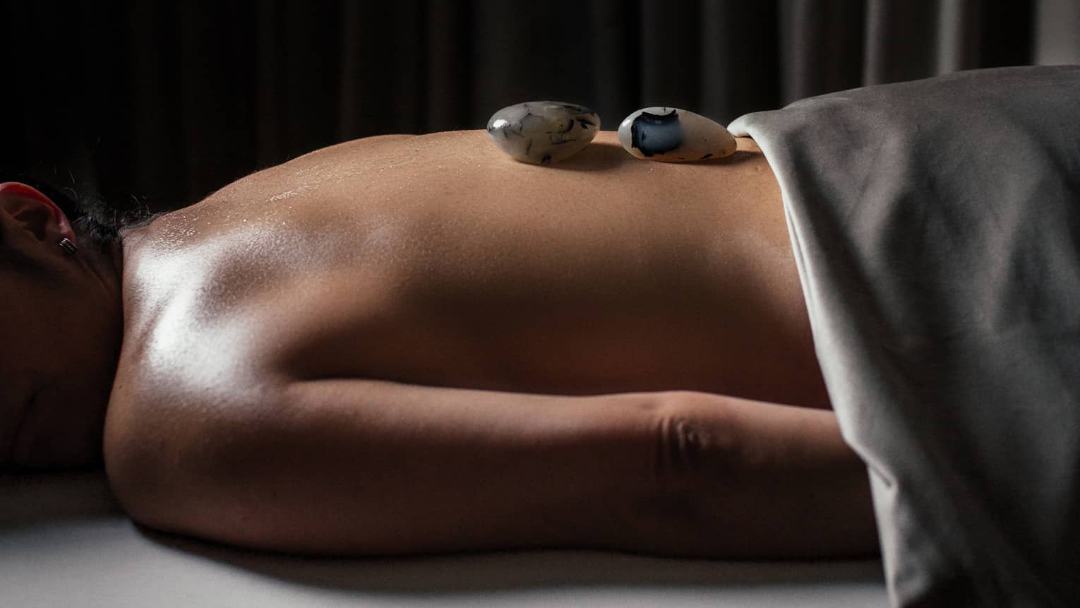 A woman with small stones on her back in a spa treatment room.