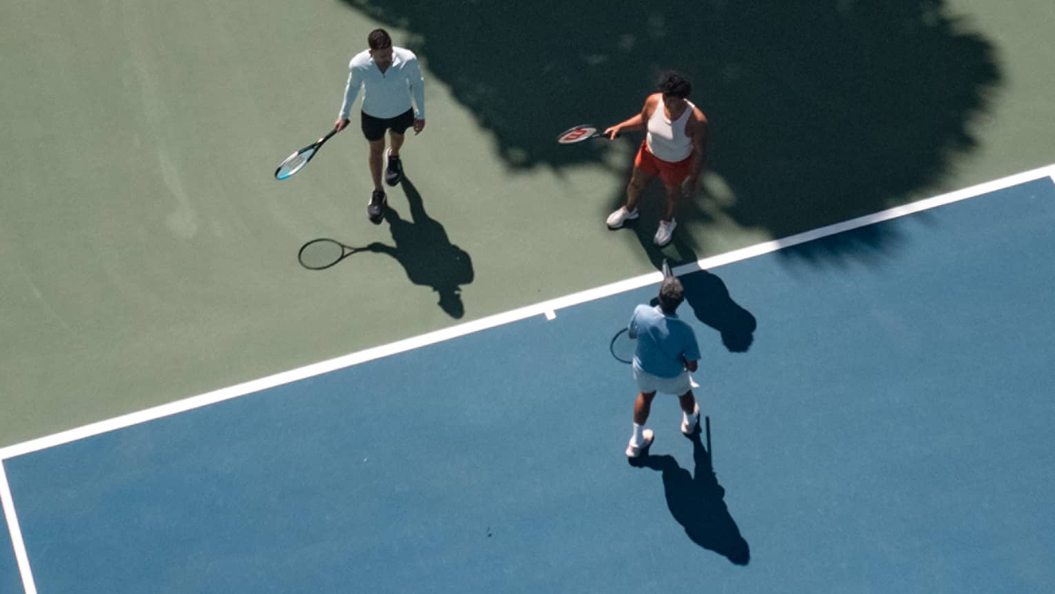 Three people holding tennis racquets on a tennis court.