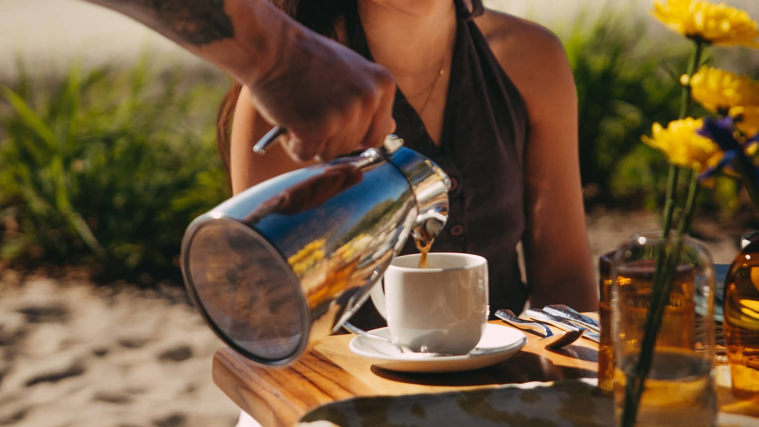 Person sits at a beach picnic while a server pours coffee
