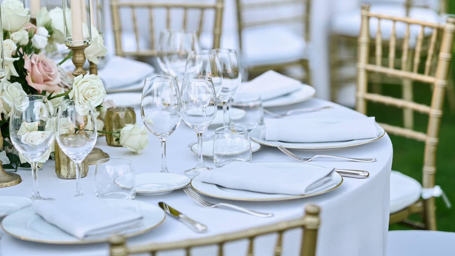 Outdoor banquet tables decorated with white floral bouquets, candles, and elegant glassware