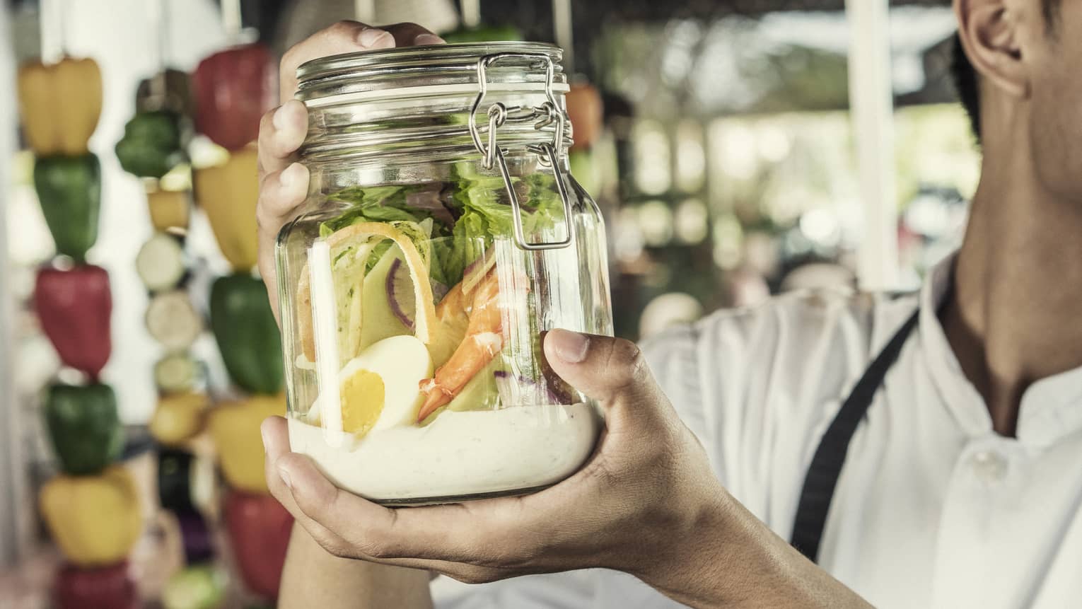 A chef shakes a caesar salad in a glass jar with some dressing