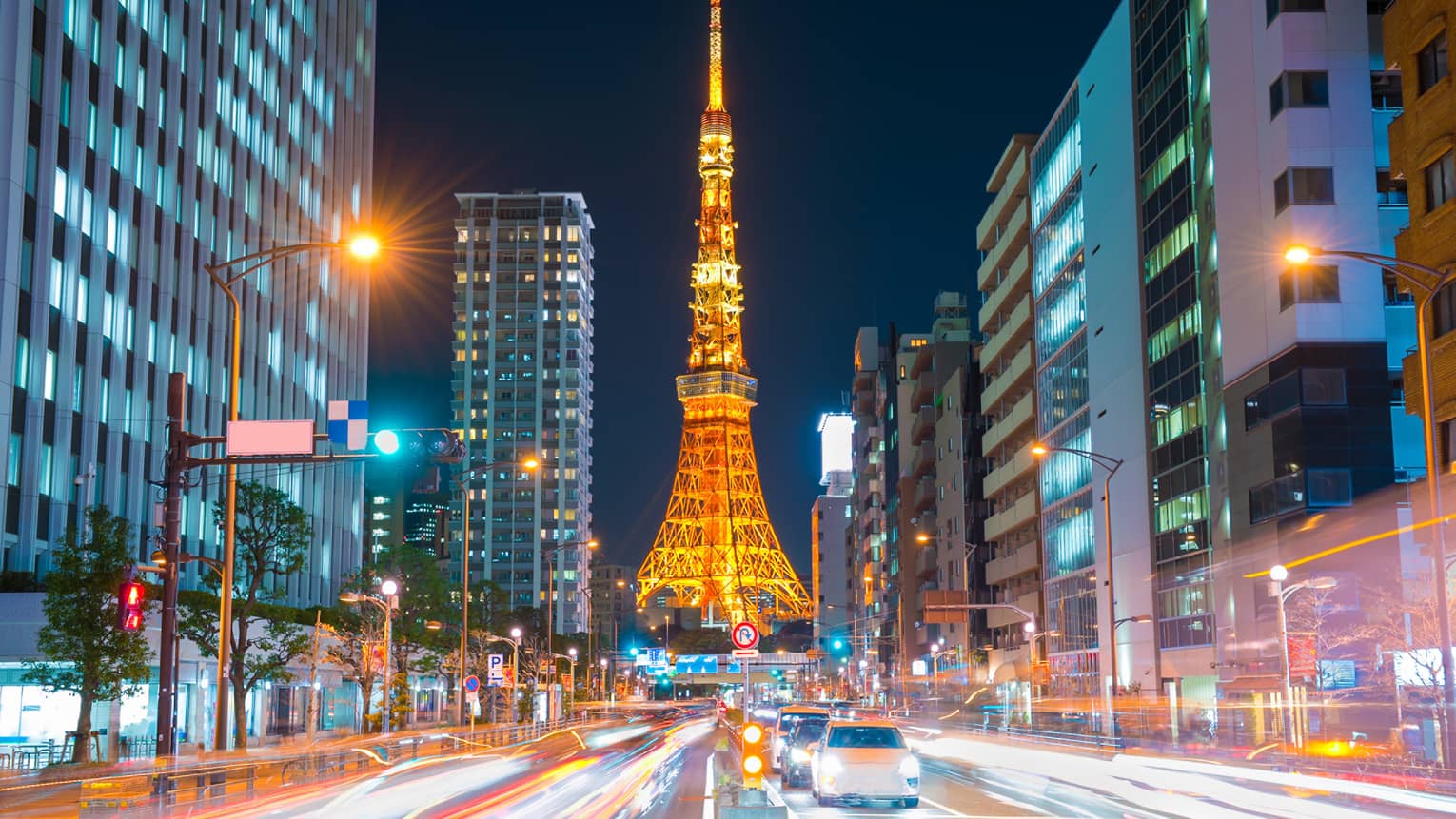 Long view down a brightly-lit street, the Tokyo Tower at the bottom, glowing in orangey hues against an inky-black sky.