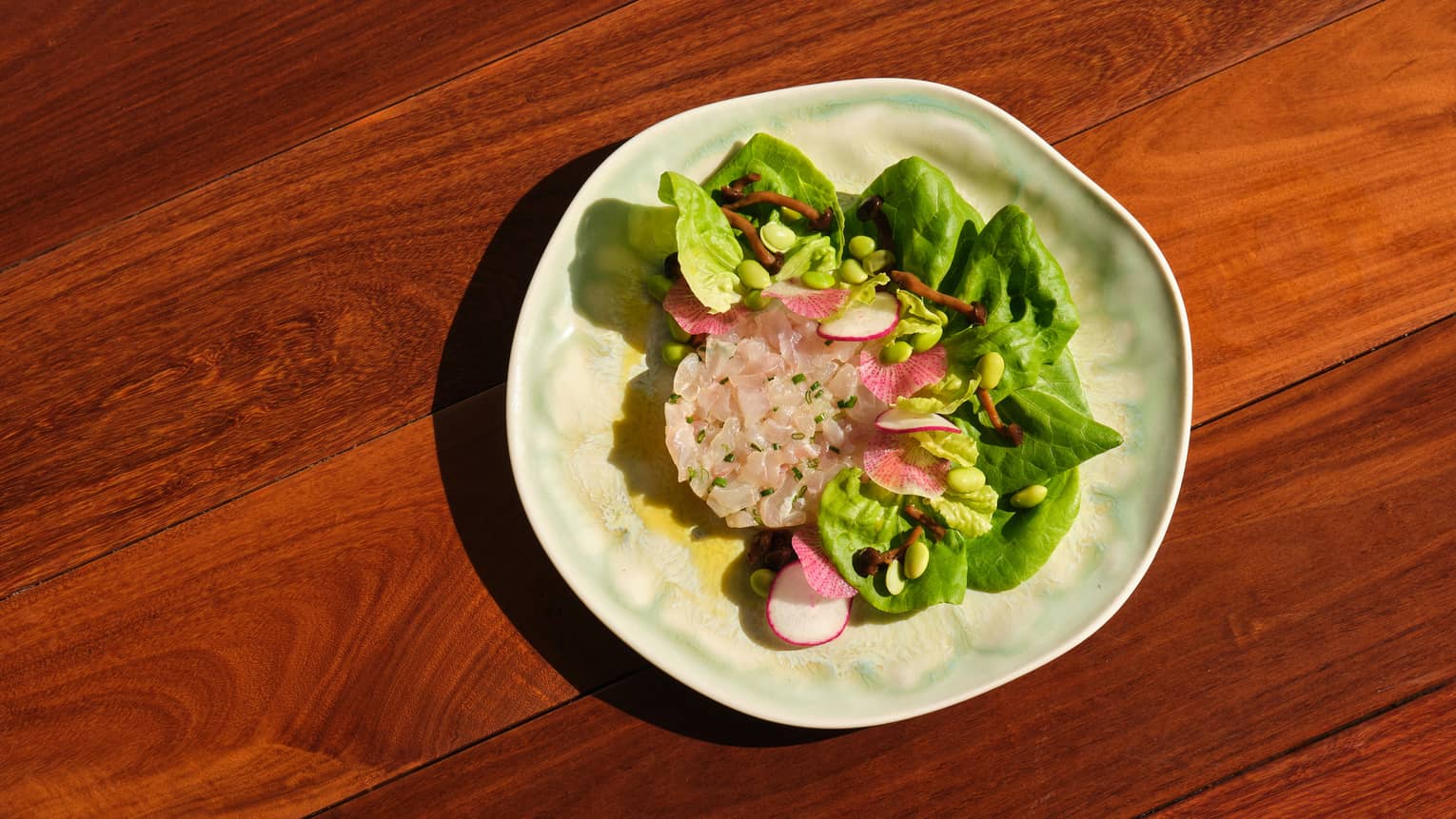 Hamachi tartare served with bibb lettuce, edamame wakame seaweed, pickled mushrooms and passion fruit dressing on a stoneware plate